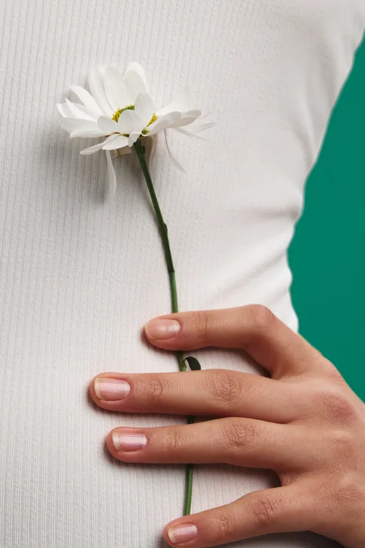 asian woman gently holds a white flower against a soft knit fabric, creating a calm closeup that conveys serene elegance, natural light, and subtle beauty.