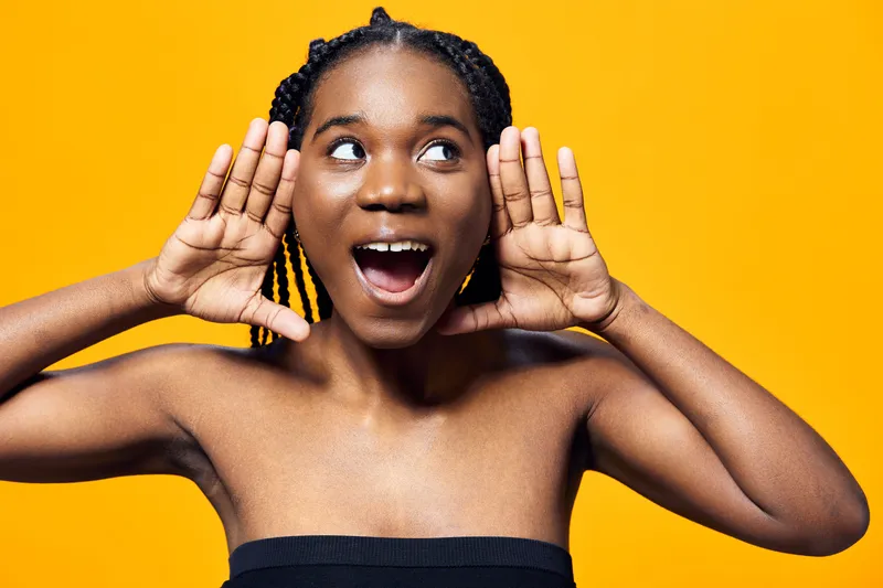 Happy African girl with braided hair expressing excitement and joy against a bright yellow background, showcasing vibrant energy and playful spirit