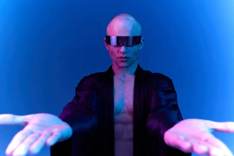 Futuristic man with sunglasses extending his hands, wearing a flowing black robe, exuding confidence and mystery in a blue-lit environment.