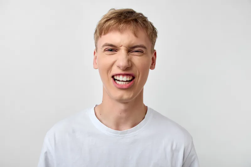 Man with a dramatic grimace showing teeth, wearing a white t-shirt in a clean studio, conveying bold emotion, playful energy and striking visual impact for stock imagery.