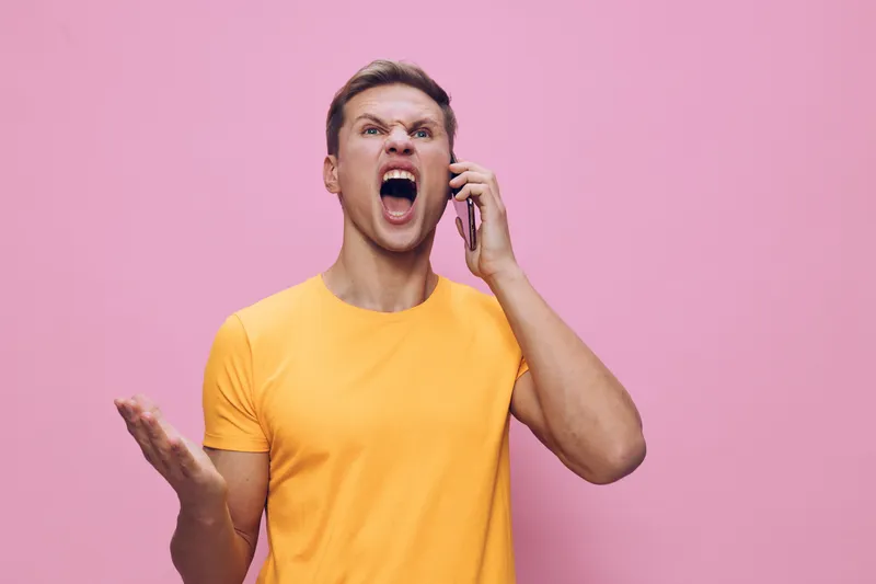 angry man shouting hold smartphone yell in yellow tshirt pink background frustrated stressed emotion concept digital detox communication