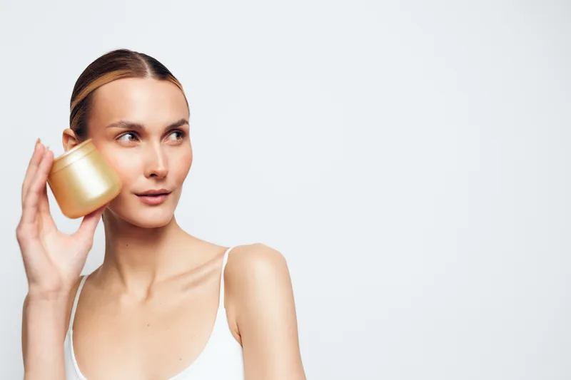 Young woman holding a small cup to her ear, listening with calm expression, beauty portrait isolated on white background, smooth skin, minimal studio style close up.