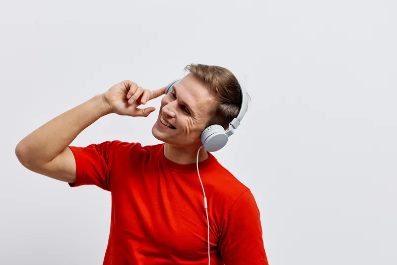 Smiling woman wearing red t-shirt listening to music with headphones and looking away, isolated on plain white background. Studio portrait conveying relaxation, enjoyment, leisure, happiness, music ap