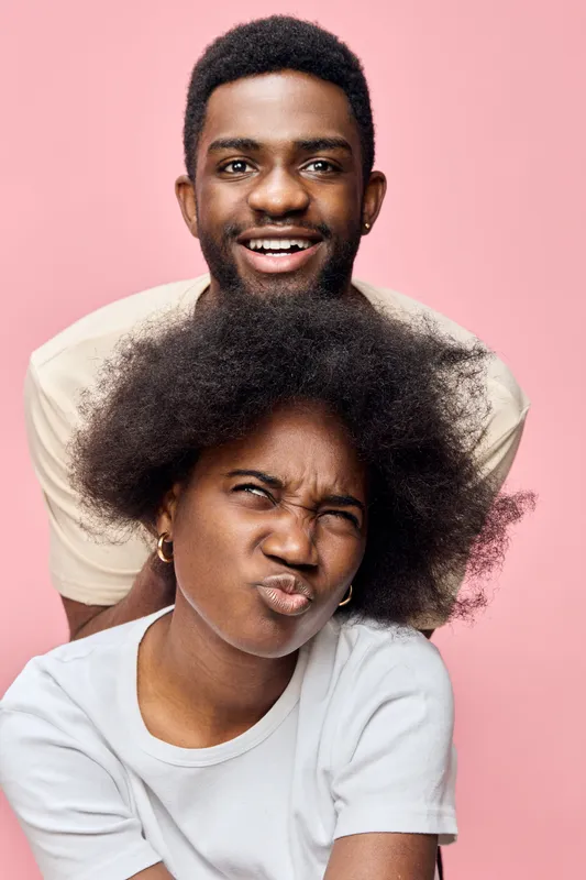 Young Afro American couple with joyful expressions, vibrant colors, playful poses, contemporary style on a pastel pink background, ideal for lifestyle imagery