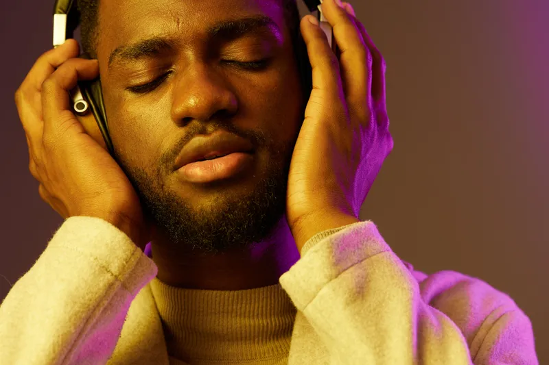 Young Black man enjoying music with headphones, eyes closed, expressing joy and relaxation against a colorful gradient background