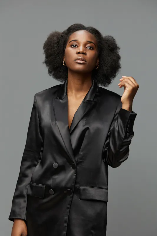 Elegant African woman in a satin black blazer, conveying confidence and sophistication against a neutral background