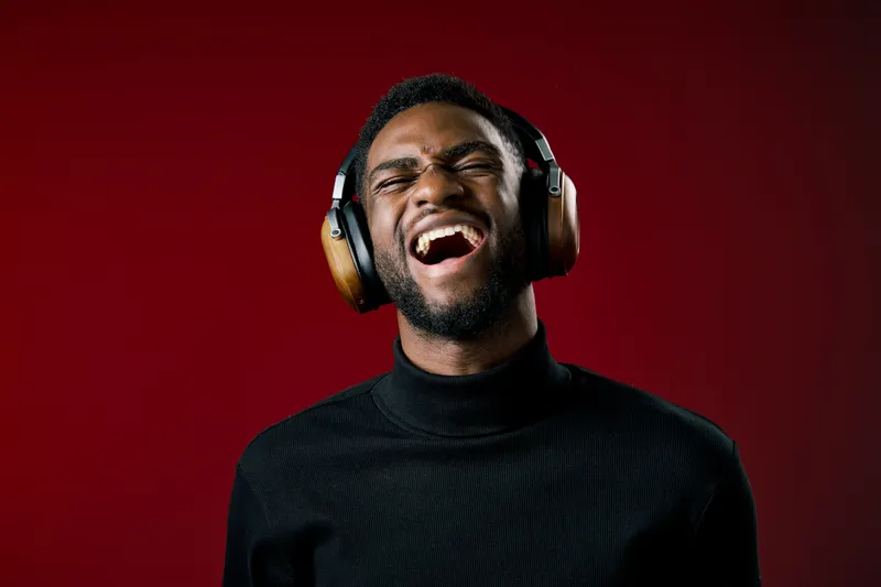 Joyful African man with headphones, passionately enjoying music against a vibrant red background, expressing happiness and relaxation