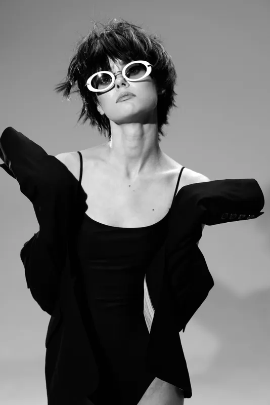 Black and white portrait of stylish woman wearing sunglasses and loose jacket with short hair and confident pose