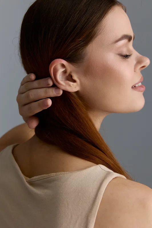 beauty woman with clear skin and natural makeup poses with closed eyes in a minimalistic beige outfit against a neutral gray background
