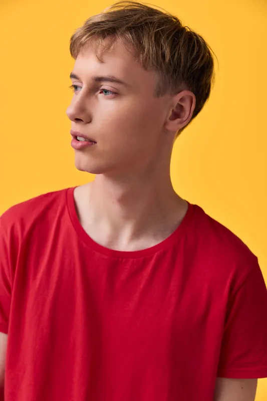 Young male in a red shirt against a bright yellow background, looking to the side, casual studio shot for fashion, lifestyle, color styling and contemporary mood.