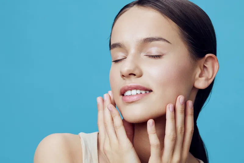 Young woman with flawless skin expressing joy against a blue background, highlighting beauty, skincare, and happiness in a fresh and vibrant style