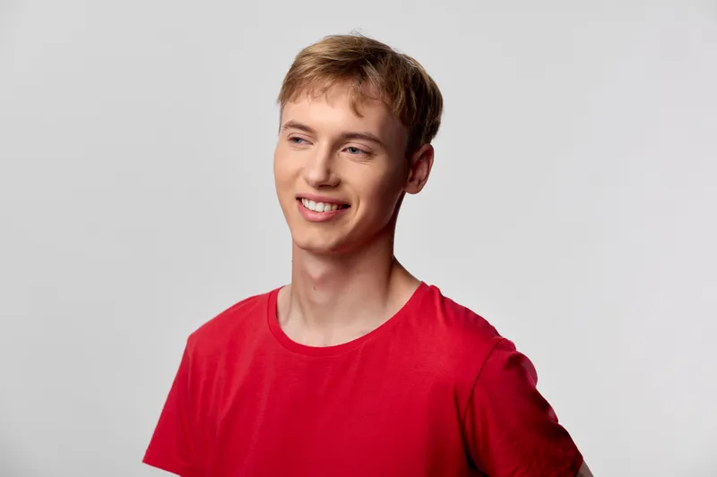 Young male with a bright smile wearing a red shirt in a casual studio setting, relaxed pose and natural lighting, showcasing approachable confidence for lifestyle and fashion imagery