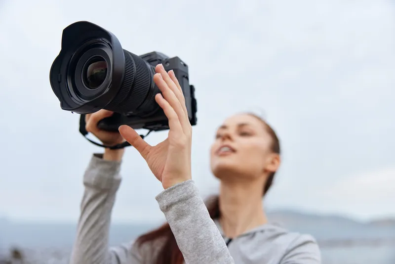 Young woman capturing nature with a camera, showcasing her photography passion in an outdoor setting with a cloudy sky