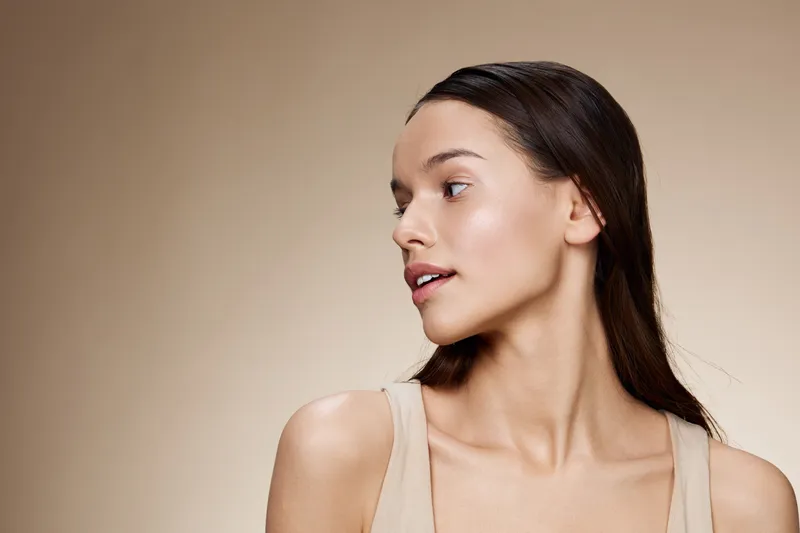 Beautiful young woman with natural makeup and healthy skin, showcasing a profile view against a neutral background, emphasizing beauty and confidence