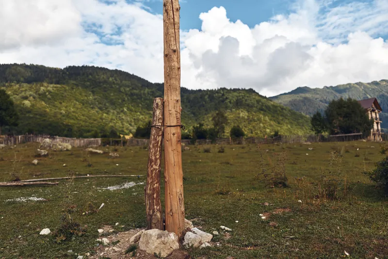 Landscape, field, lone wooden post stands in a rugged rural scene with distant mountains and a small ruin beneath a bright sky, weathered textures and open space