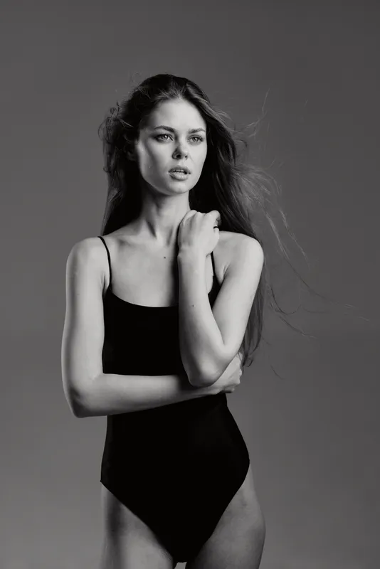 Black and white portrait of a serious woman in black apparel with flowing hair, expressing thoughtfulness and elegance.