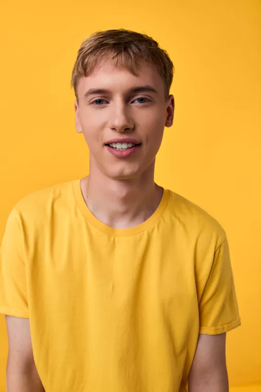 Smiling young man wearing a yellow shirt against a bright yellow background, casual studio look with headshot vibe, ideal for lifestyle, fashion, or upbeat branding imagery.