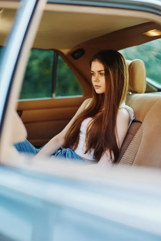 Thoughtful young woman with long hair sitting in a car, reflecting on life, capturing emotions in a serene setting.