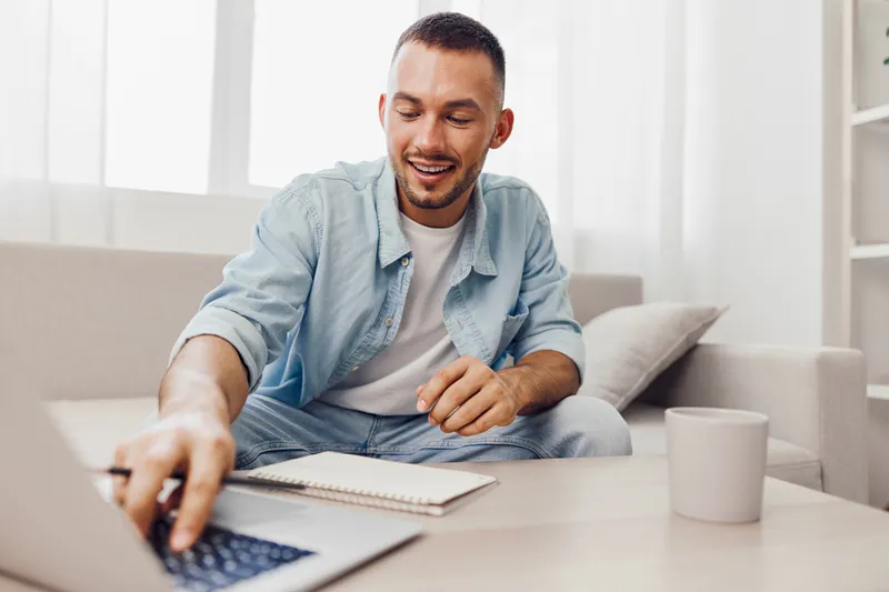 Engaging man working on laptop in modern living room, showcasing productivity and comfort. Bright space inspires creativity and motivation.