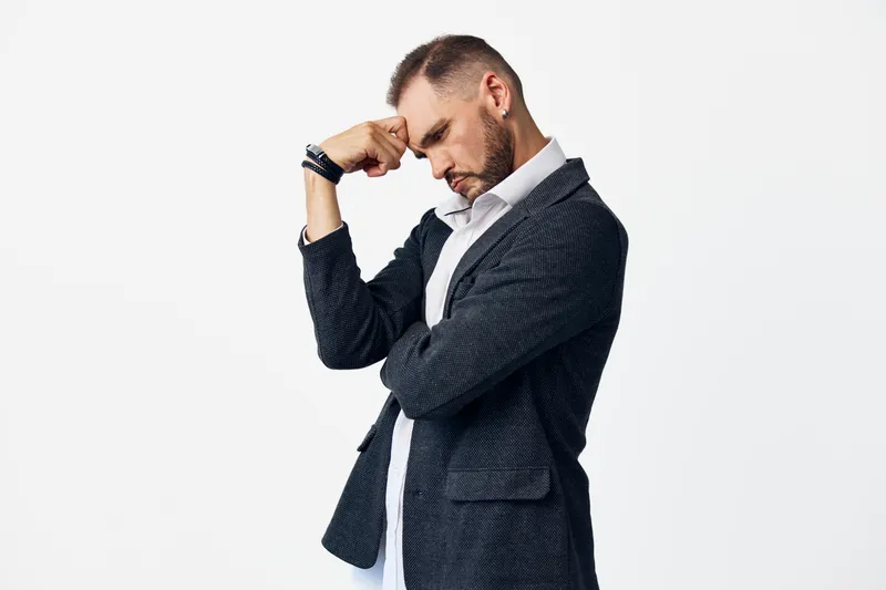 A professional man in business attire stands against an isolated colored background, exuding confident focus, deliberate posture, and subtle introspection.