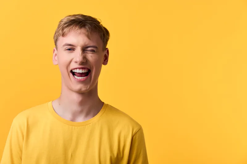 Laughing man in a yellow shirt stands against a vivid yellow background, radiating happiness, energy and warmth under bright studio lighting, creating a candid, upbeat mood for lifestyle or