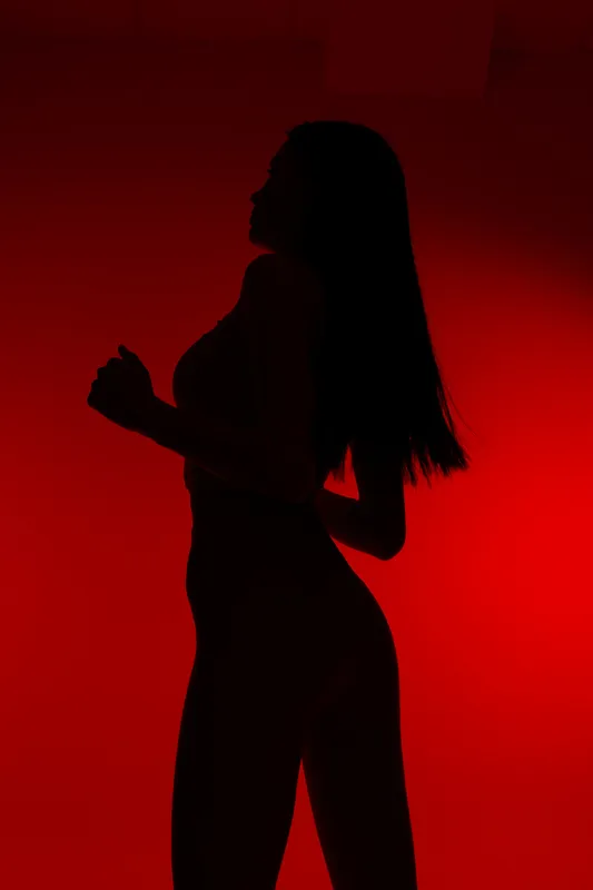 Silhouette of a sport fitness woman running against a red background, highlighting strength, motion, and endurance in a dynamic athletic pose.