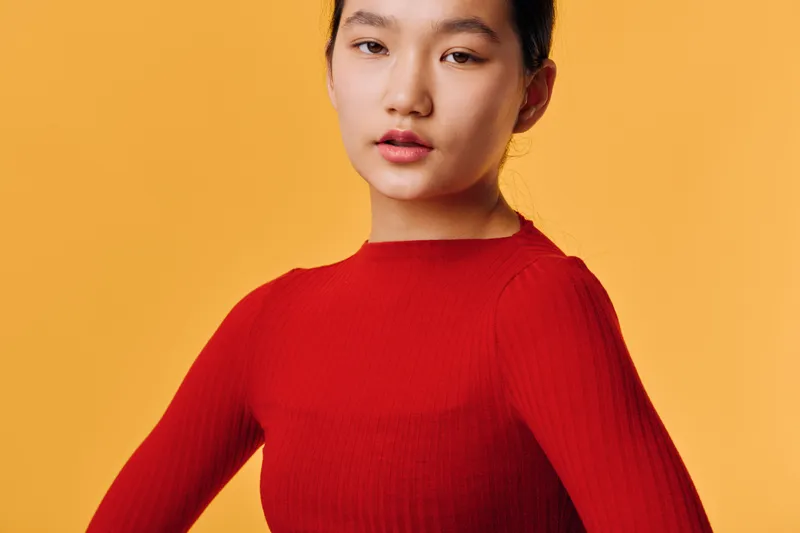 Young woman in red sweater posing confidently against yellow background, studio portrait with natural expression and casual style for fashion or lifestyle content.