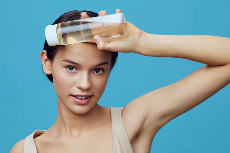 Young model holding a bottle of facial oil against a blue background, promoting skincare, natural beauty, and self care concepts for healthy skin