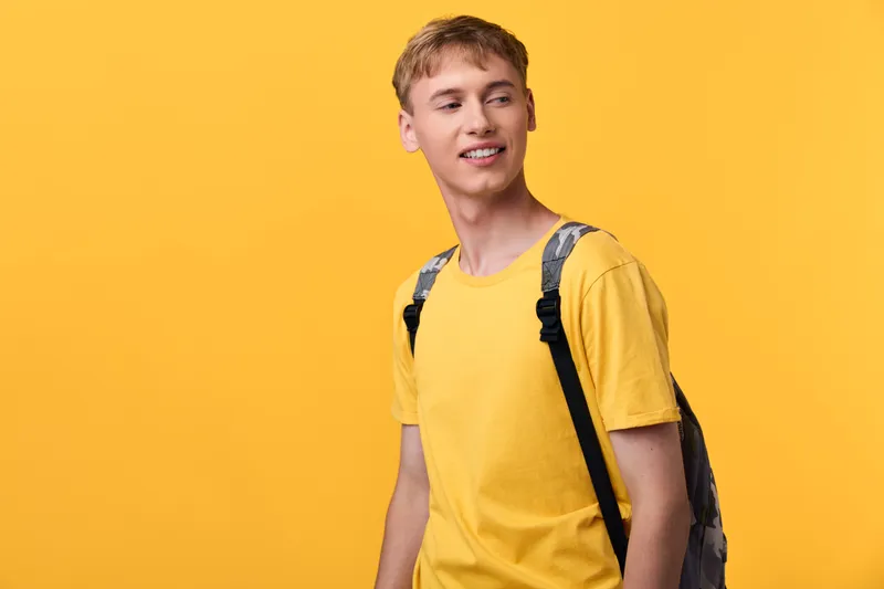 Youthful male student in a bright yellow t shirt with a backpack, standing against a bold yellow backdrop. Casual style, everyday fashion, upbeat energy and ready for class, study, or campus