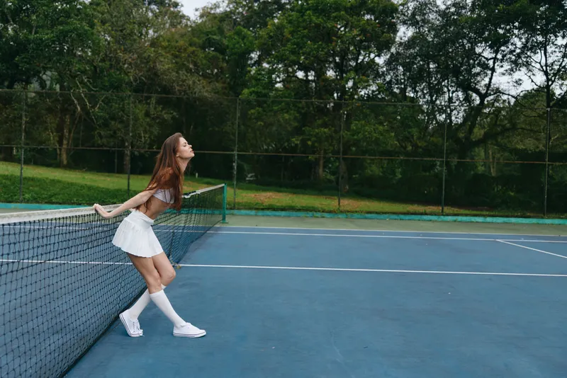 Energetic young woman in white tennis outfit joyful on outdoor court emphasizing healthy lifestyle and sports enthusiasm