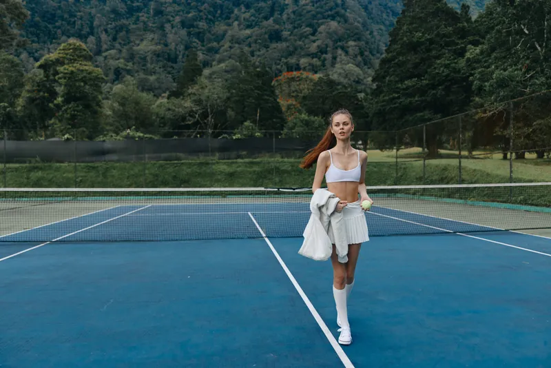 Young athletic woman in sporty outfit walking on tennis court during sunny day, showcasing healthy lifestyle and active leisure