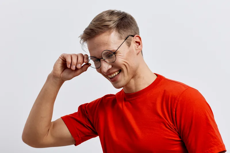 smiling man wear glasses touch head look down happy casual red t-shirt isolated on plain white background cheerful lifestyle concept