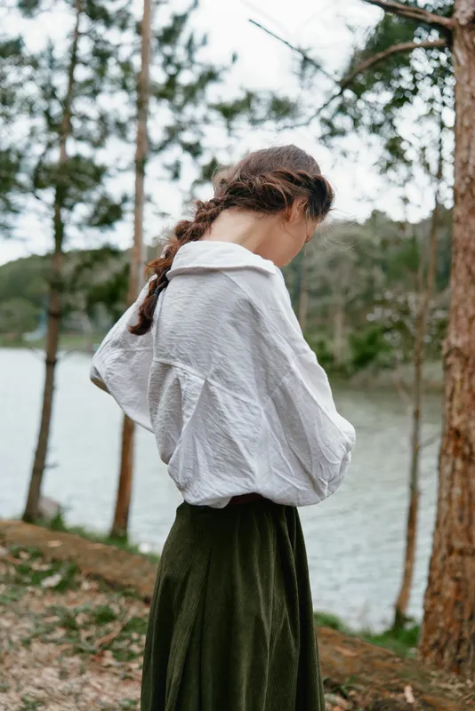 Young woman in a casual outfit with a white shirt and green skirt against a serene natural background by a lake, showcasing tranquility and reflection