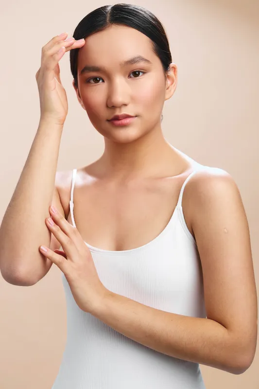 Asian woman in a light tank top poses confidently against a soft beige studio backdrop, exuding calm elegance and focused professionalism suitable for lifestyle and business themed imagery.