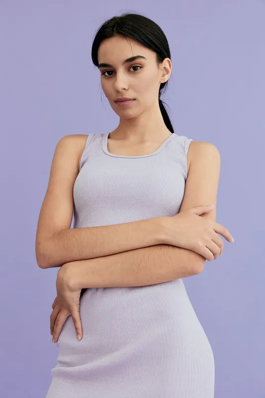 Young woman in a lavender dress posing with crossed arms against a soft purple background, showcasing calm expression and minimalist style in studio lighting.