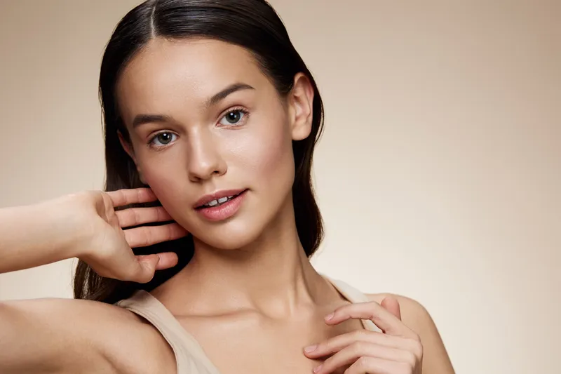 Young woman with natural beauty showcasing healthy skin and a relaxed expression against a soft beige background, ideal for beauty and skincare concepts