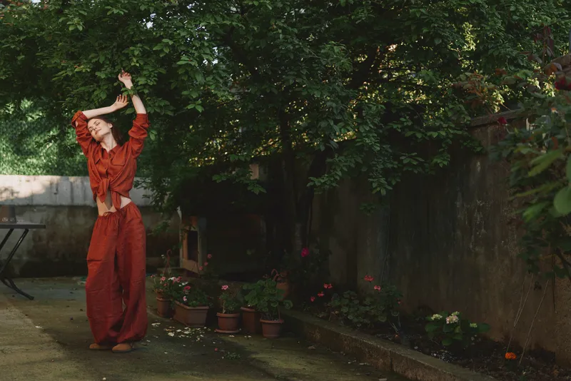 Woman in a rust jumpsuit dancing in a garden, joyful movement outdoors, natural light, candid lifestyle moment amid lush greenery and flowers