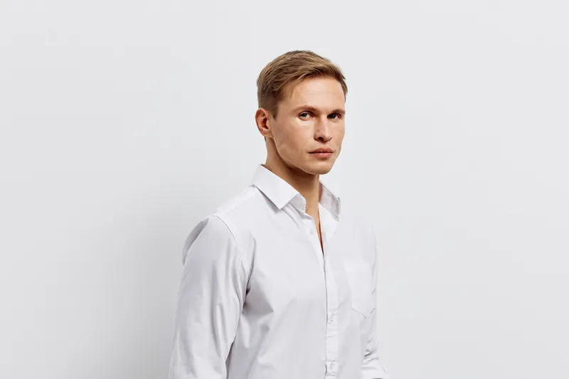 serious young caucasian man wearing white shirt looking at camera with thoughtful expression isolated on plain light grey background digital detox concept