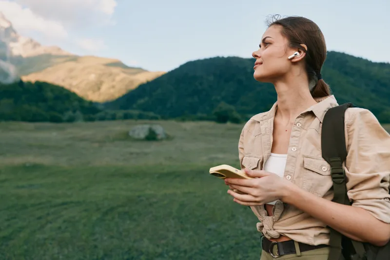 A woman explorer stands outdoors with a notebook and backpack, gazing toward distant hills. A lifestyle scene about curiosity, adventure, and personal growth in nature.