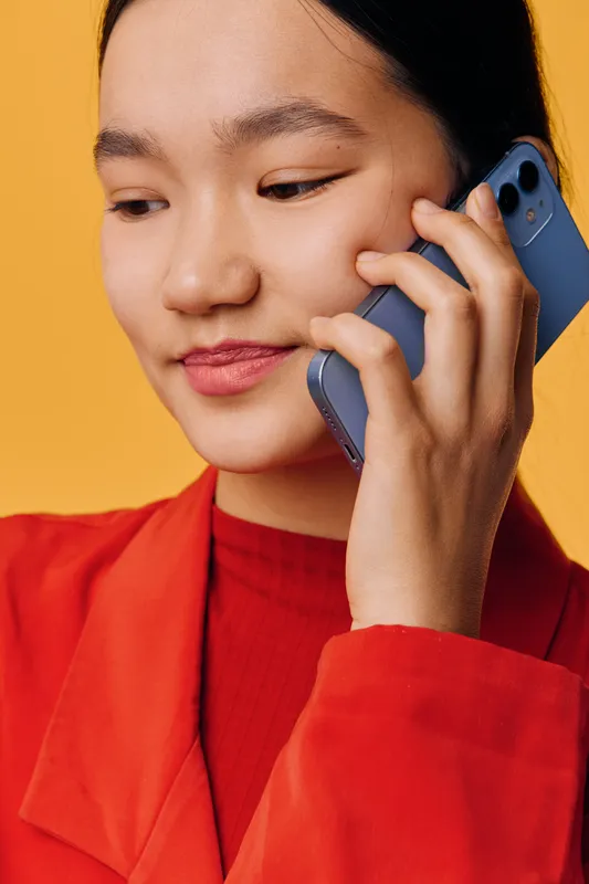 Woman talking on smartphone with smile, wearing red jacket and red sweater on yellow background. Closeup portrait of female person with casual style and relaxed expression.