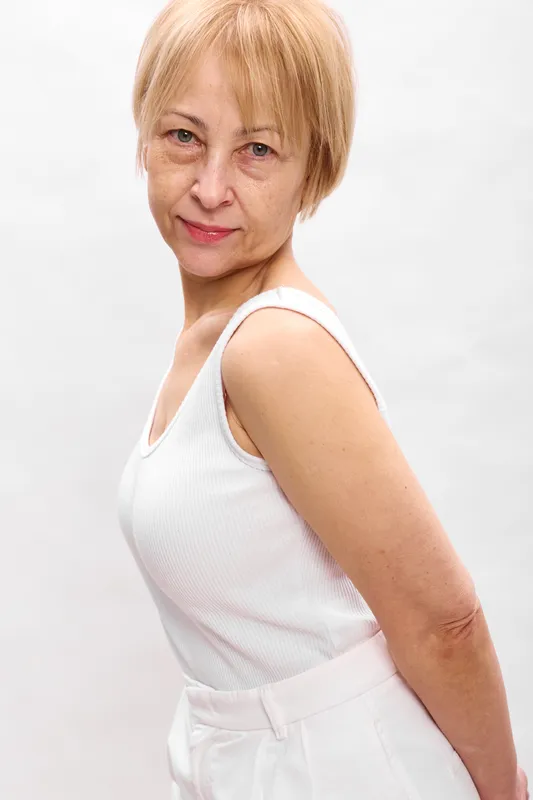 Woman portrait, blonde hair, smile, white sleeveless top, studio setting, calm eyes to camera, soft even light, neutral background, relaxed posture, minimal fashion