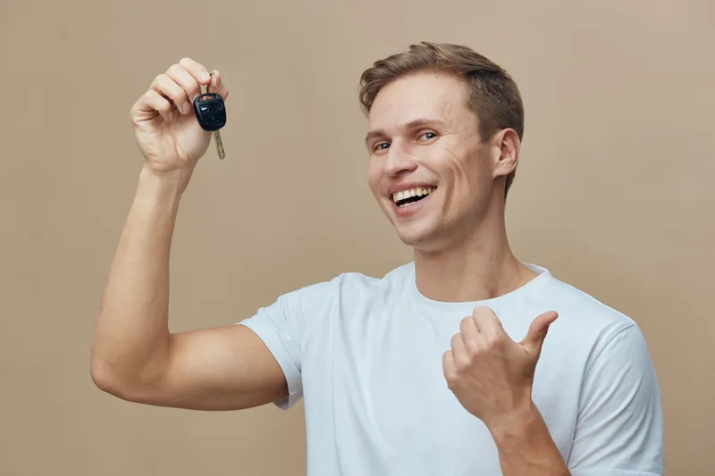 smiling young caucasian man hold car keys wear white t shirt show thumb up gesture excited happy face on beige background digital nomad concept