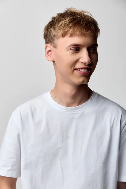 Young man wearing a white t shirt with a bright smile in a clean studio setting, casual style and relaxed pose, emphasizing contemporary fashion and everyday confidence.