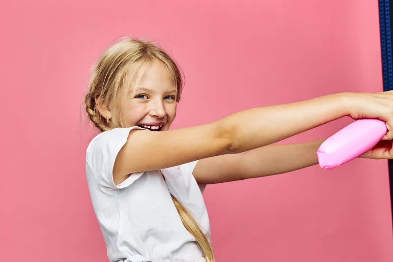 Happy smiling girl with long blonde hair in a white t-shirt playing with pink toy against pink background. Studio portrait with joyful expression and playful concept of childhood.