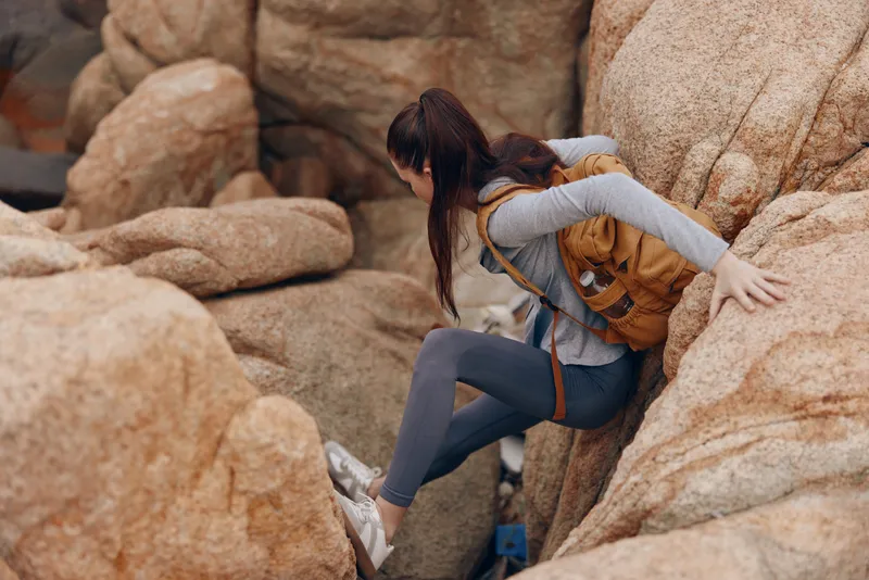 A determined young woman with a backpack navigating rocky terrain, showcasing adventure, perseverance, and exploration in a natural setting