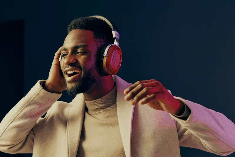 Young man enjoying music with headphones, smiling in a stylish coat, against a colorful background Perfect for concepts of relaxation and happiness