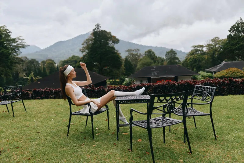 Young woman enjoying a healthy lifestyle while relaxing outdoors in stylish sportswear, surrounded by nature in a tranquil setting