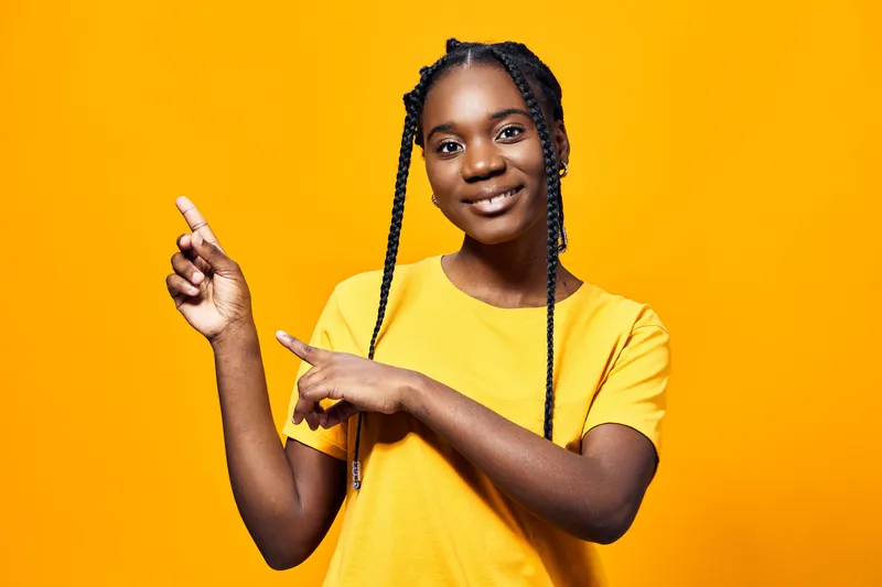 Happy young girl in a yellow shirt pointing with both hands against a vibrant yellow background, showcasing enthusiasm and positivity in a bright, cheerful atmosphere