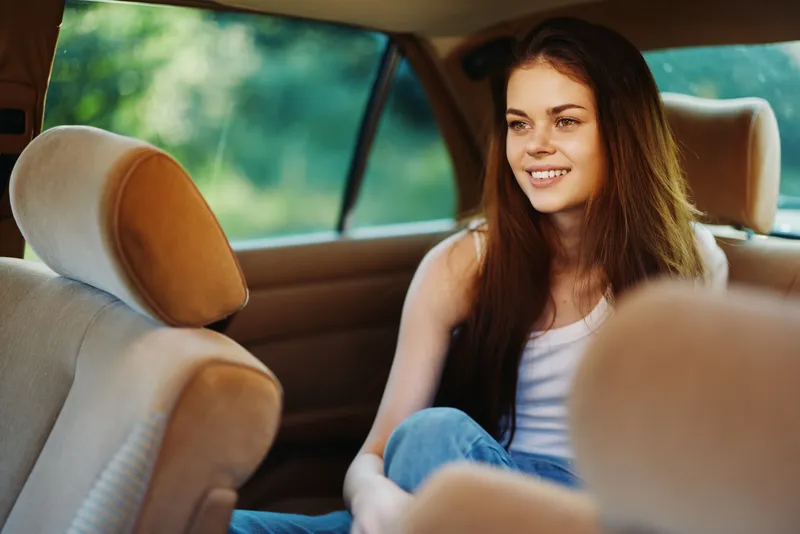 Young woman smiling in a car interior, wearing casual clothing, enjoying a sunny day, demonstrating happiness and relaxation in a natural setting.