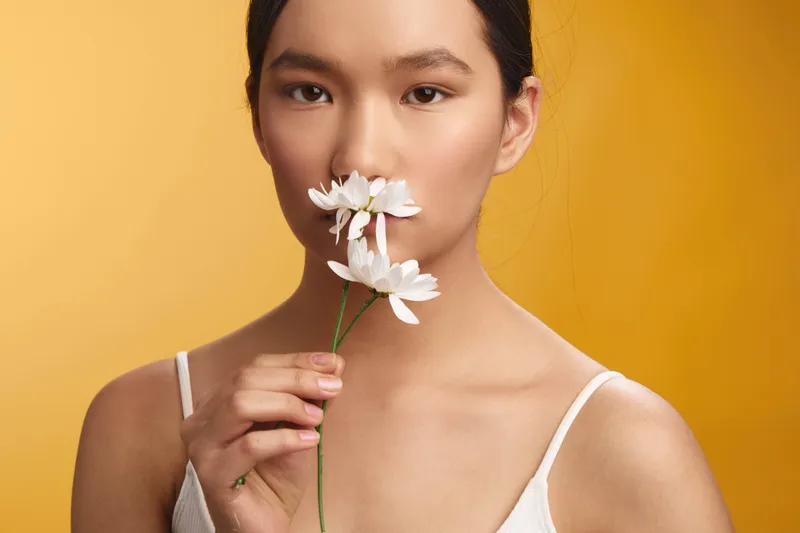asian woman gently inhales a delicate bloom in a close up portrait with warm backdrop, soft light and calm ambiance emphasize natural beauty, serenity, and subtle fashion essence